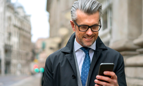 Homme portant des lunettes et regardant son smartphone dans la rue