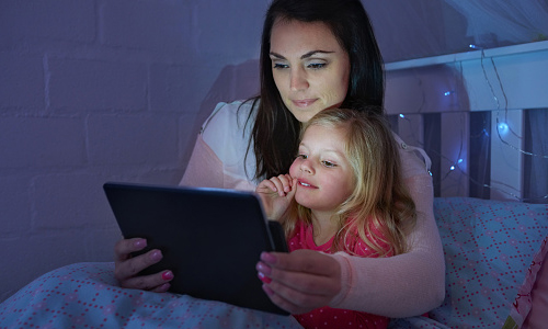 Jeune maman et sa fille regardant une tablette en lumière tamisée